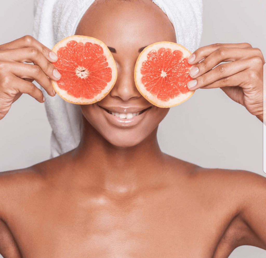 A woman holding grapefruit slices in front of her eyes.