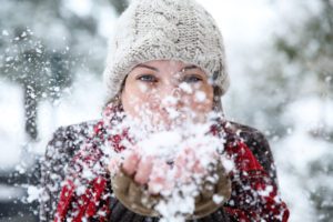 A woman blowing snow from her hands.