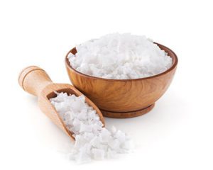 A wooden bowl filled with white rice next to a wooden spoon.