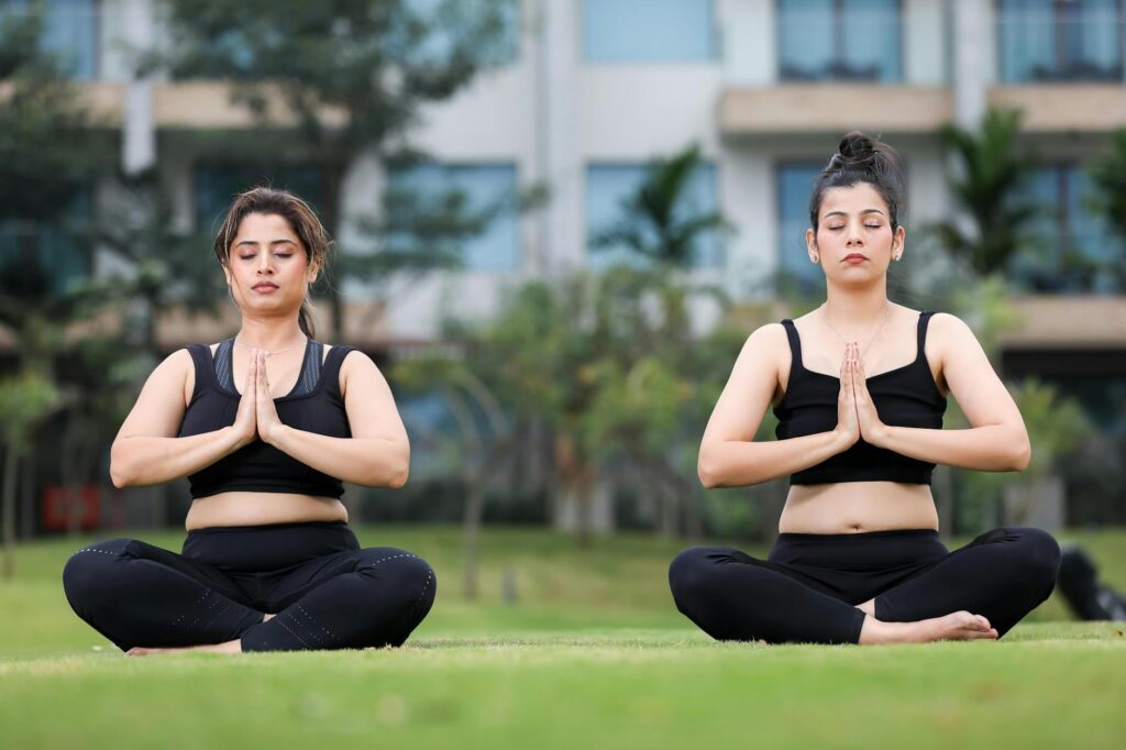 two women practicing yoga outdoors on grass